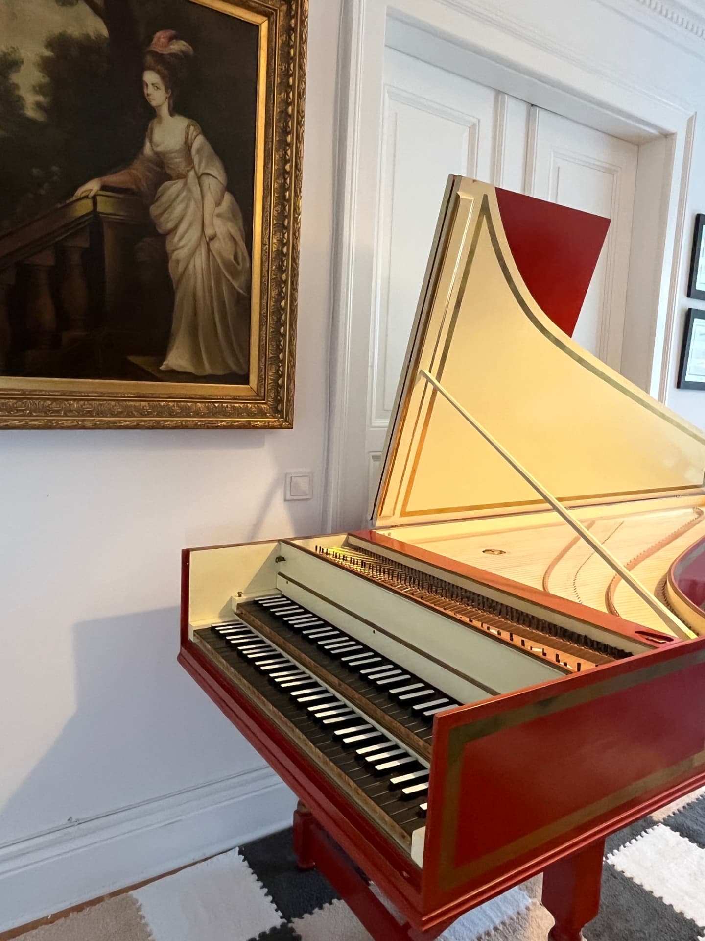 A double-manual French harpsichord in red and gold, used for Bach, Scarlatti, and early music study.